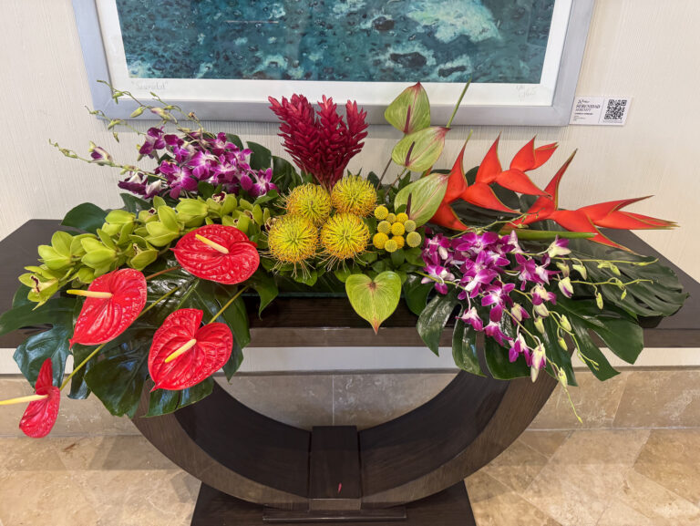 A long arrangement of anthurium, ginger and orchids on a curved console