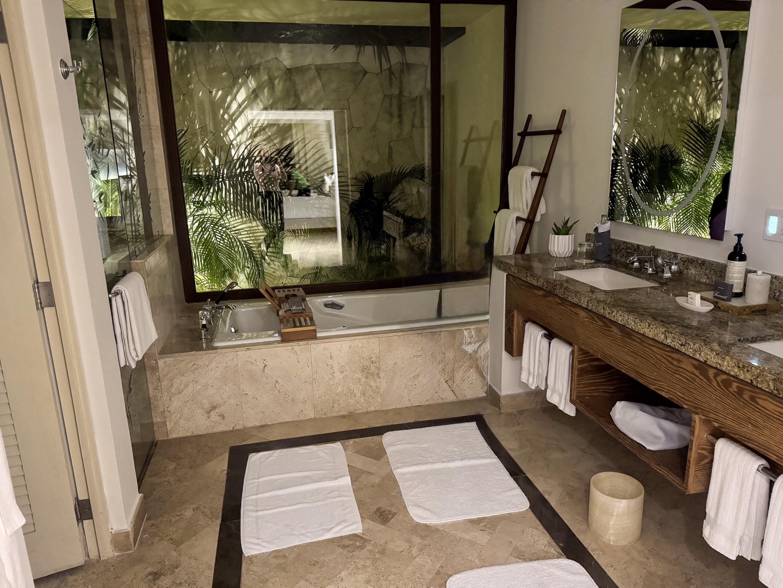 A stone bathroom with a glass shower and the garden beyond