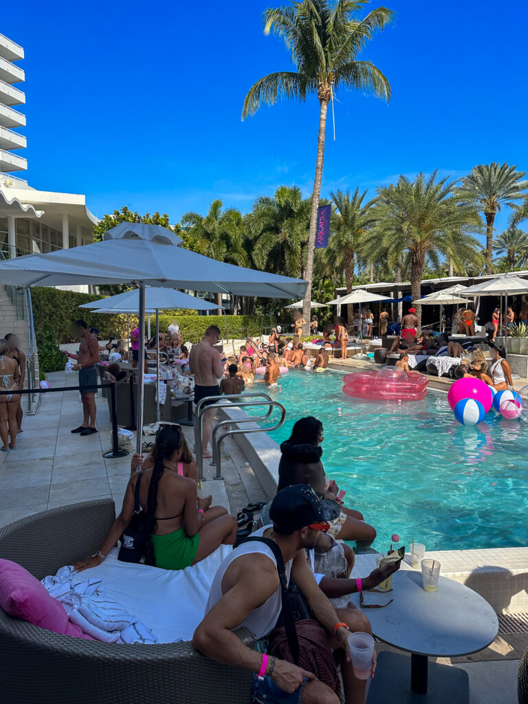Poolside daybeds and inflatable rings around the party pool beneath a tall palm