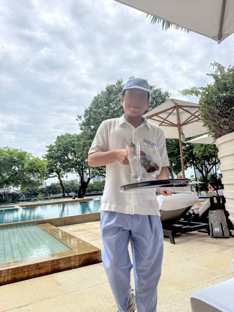A member of staff bringing a tray to the poolside under a white parasol