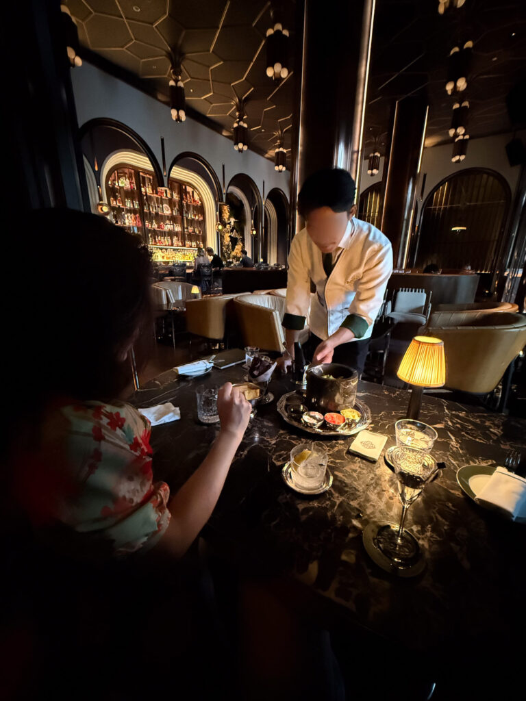 A bartender working tableside in the low-lit bar, bottles ranked behind
