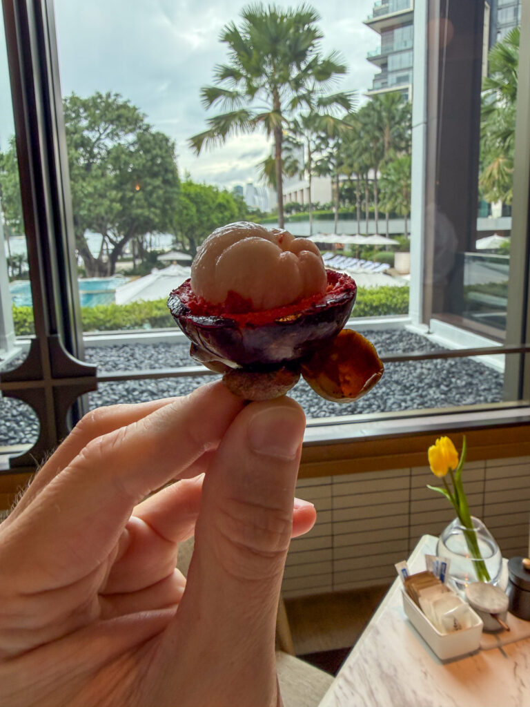 A pale dessert in a dark glass bowl on the window ledge, the pool and palms outside