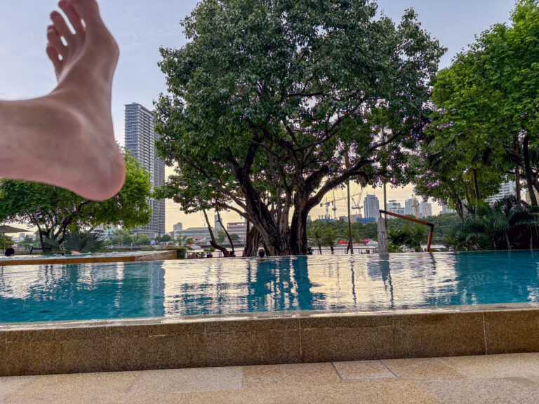 A foot raised into frame over the still pool and the trees beyond