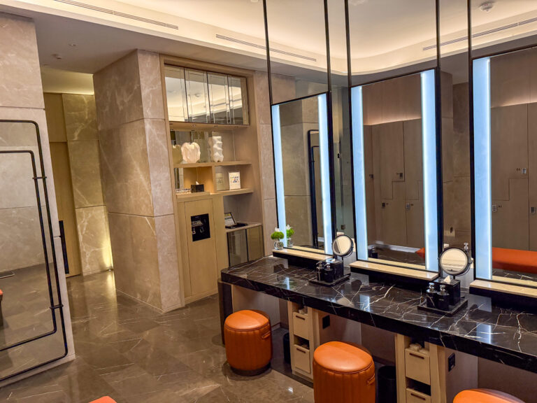 A run of lit mirrors over a dark counter, orange stools set beneath