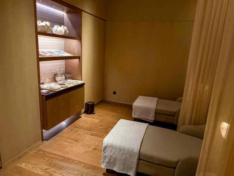 A treatment bed in a wood-lined room, folded linen on the shelves alongside