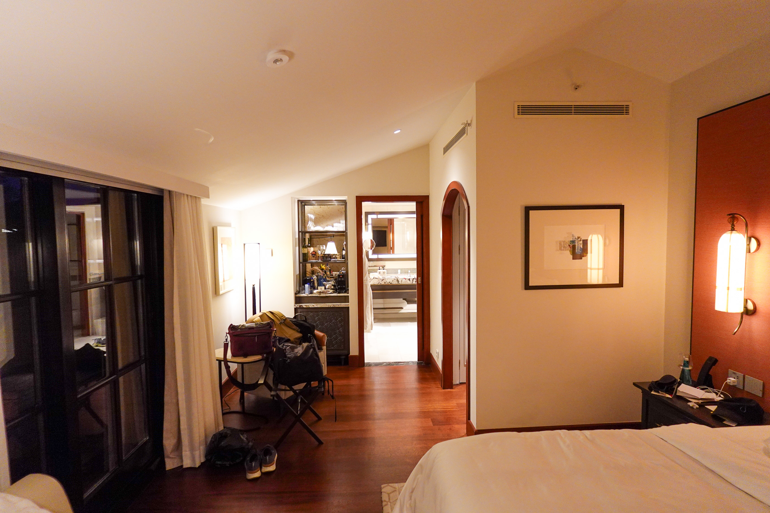 A warm, low-lit passage with framed pictures and an open door to the room beyond