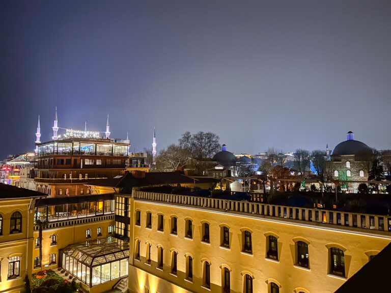 The illuminated hotel facade at dusk with the mosque glowing violet on the skyline