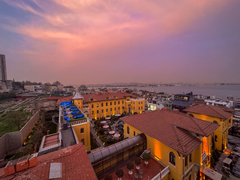 Coral cloud over the tiled roofs, with the water and the far shore beyond