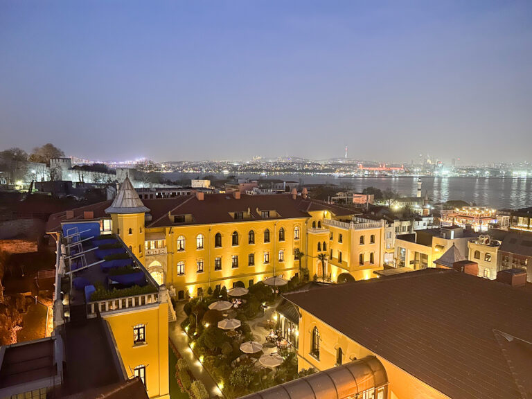 The courtyard and surrounding streets lit at dusk, the city running down to the water