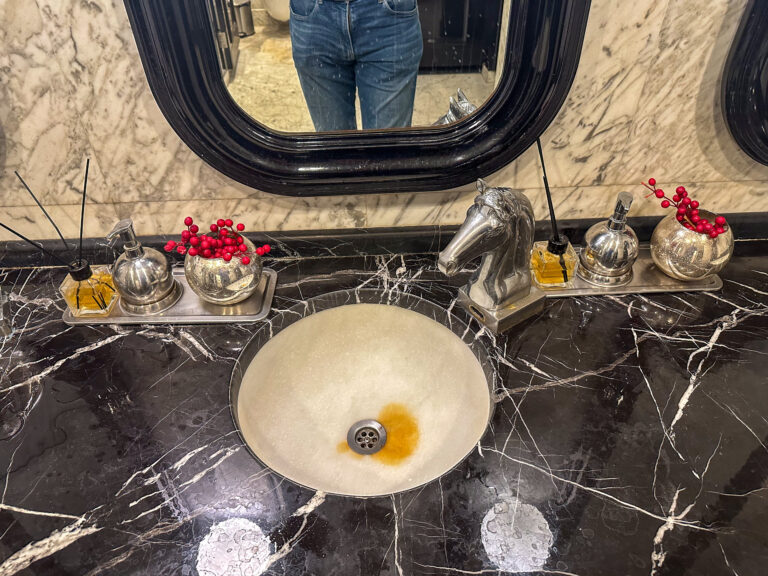 An alabaster basin set into black marble, silver fittings and a dark oval mirror above
