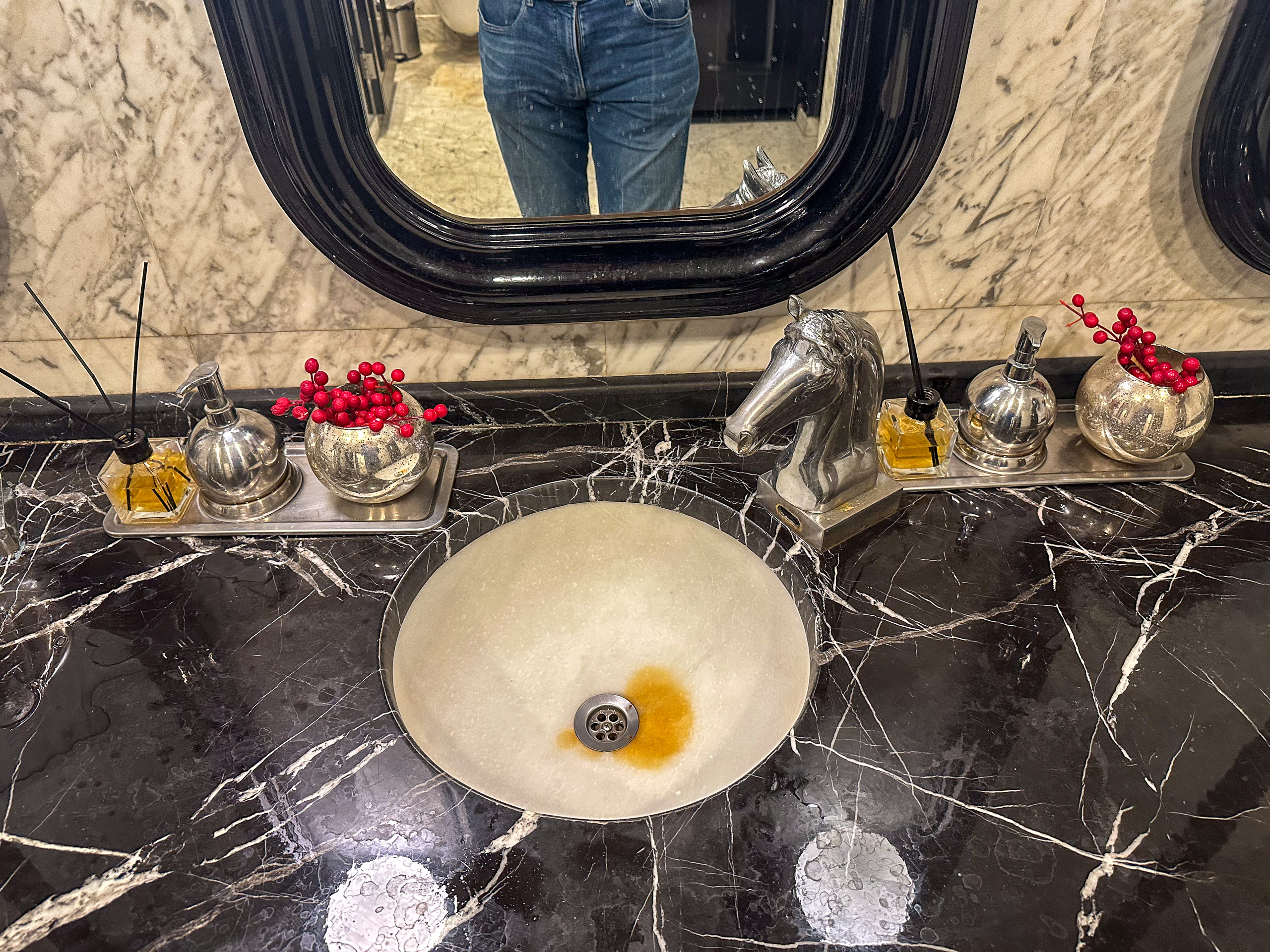 An alabaster basin set into black marble, silver fittings and a dark oval mirror above
