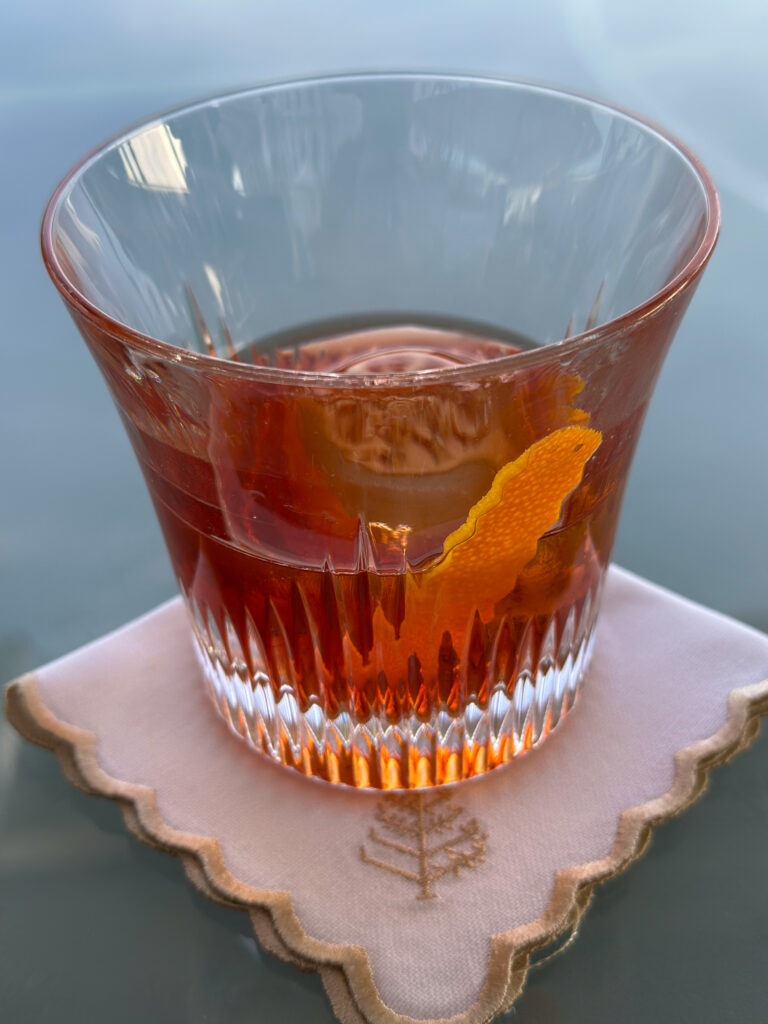 A negroni with a twist of orange in a cut glass, set on a scalloped linen coaster