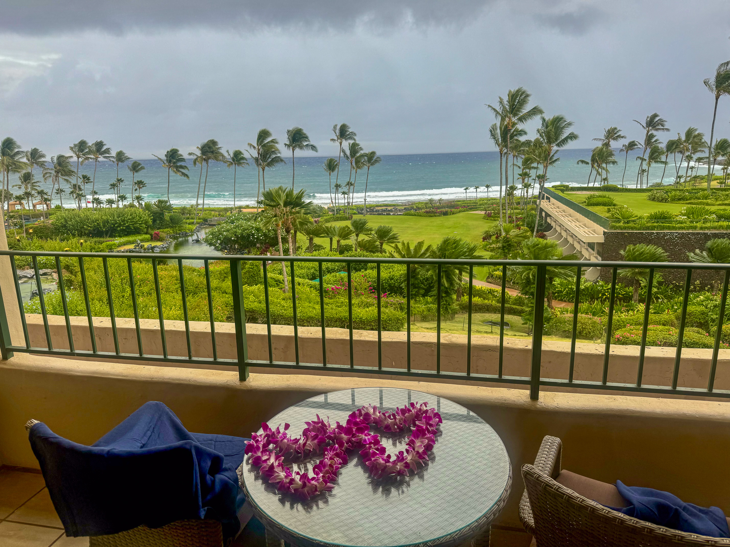 An orchid lei laid on a table on the lanai, the lawns and the sea past the balcony rail