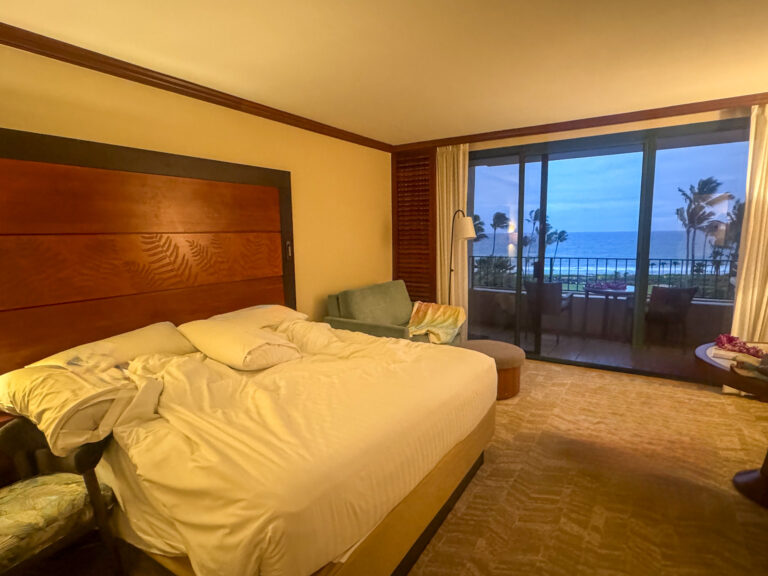 A bed made up in white, the doors open to a balcony and the water beyond
