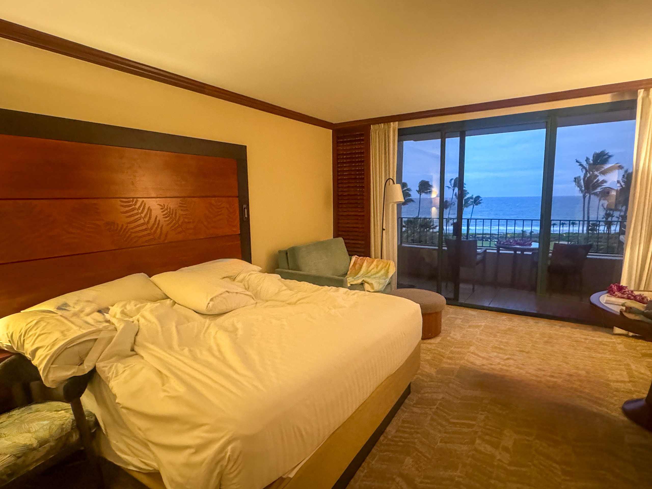 A bed made up in white, the doors open to a balcony and the water beyond