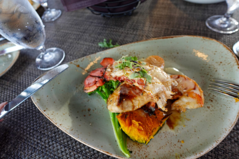 A fillet on a grey plate with vegetables and a spoon of sauce