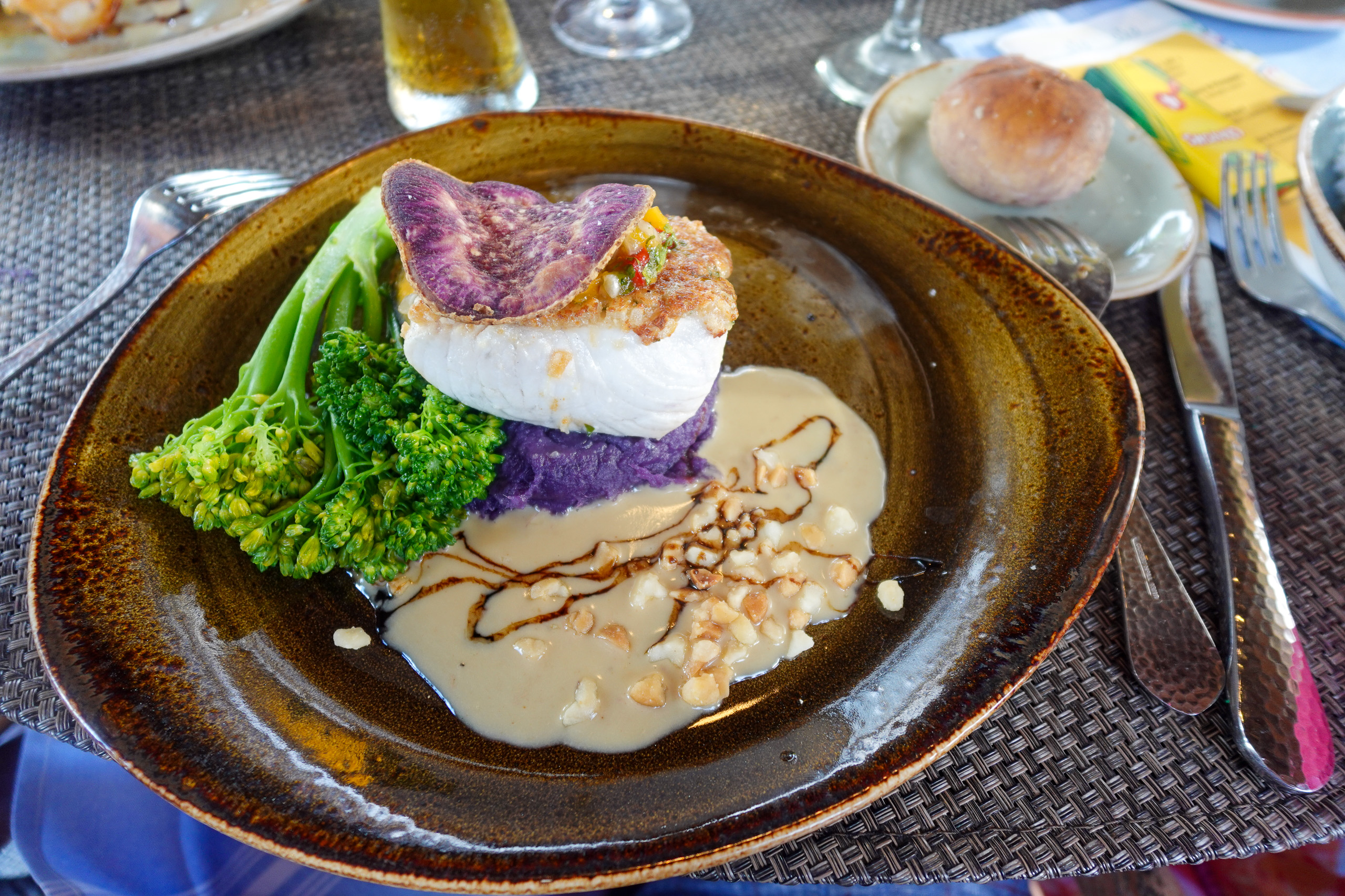 A dressed dish in purple and white on dark stoneware, a leaf salad alongside