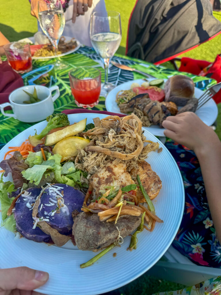 A plate carried back from the tables — pork, fish, beef and taro, and the drinks behind it
