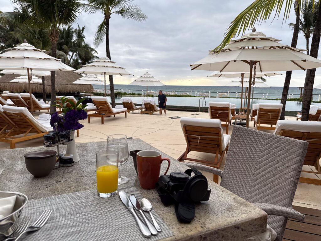 Breakfast table with juice, coffee and a camera looking out to parasols and the sea
