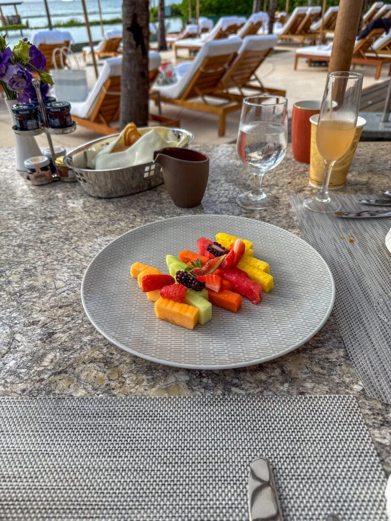 Plate of cut melon, papaya and berries on a granite table above teak loungers and sea