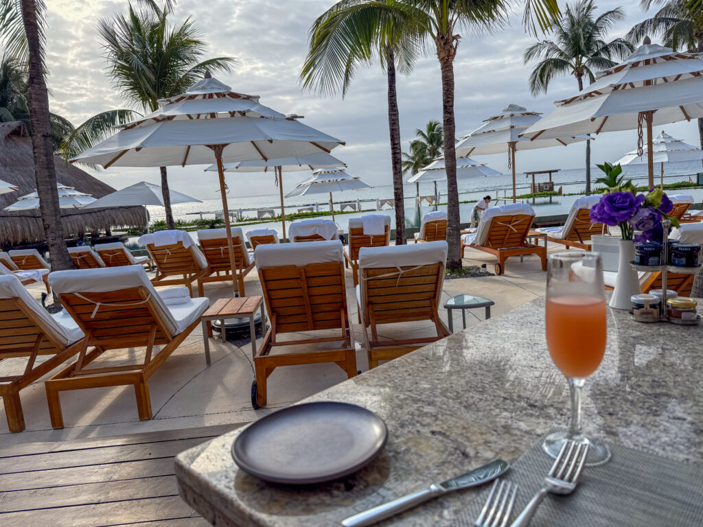 Mimosa glass and pewter plate on a granite table beside empty teak loungers at first light
