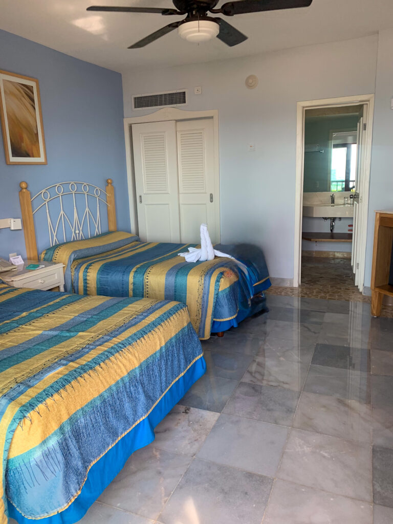 A bed with a striped cover under a ceiling fan, the walls washed pale blue