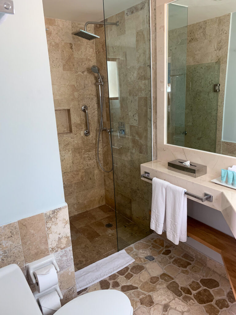 A glass shower and stone vanity, towels folded on the shelf