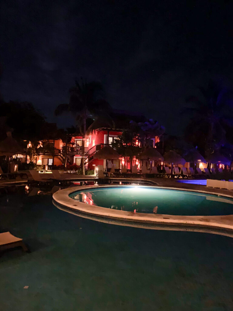 The pool lit from below, the buildings behind it washed in pink light