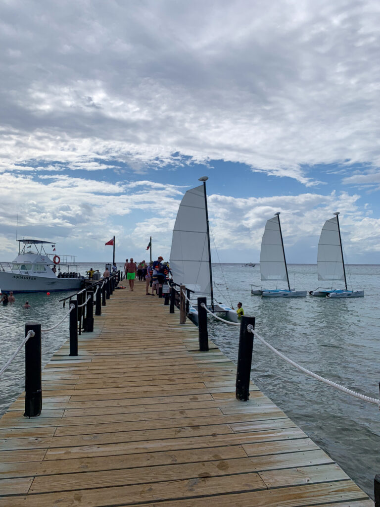 A wooden pier running out over the water, sails on the horizon