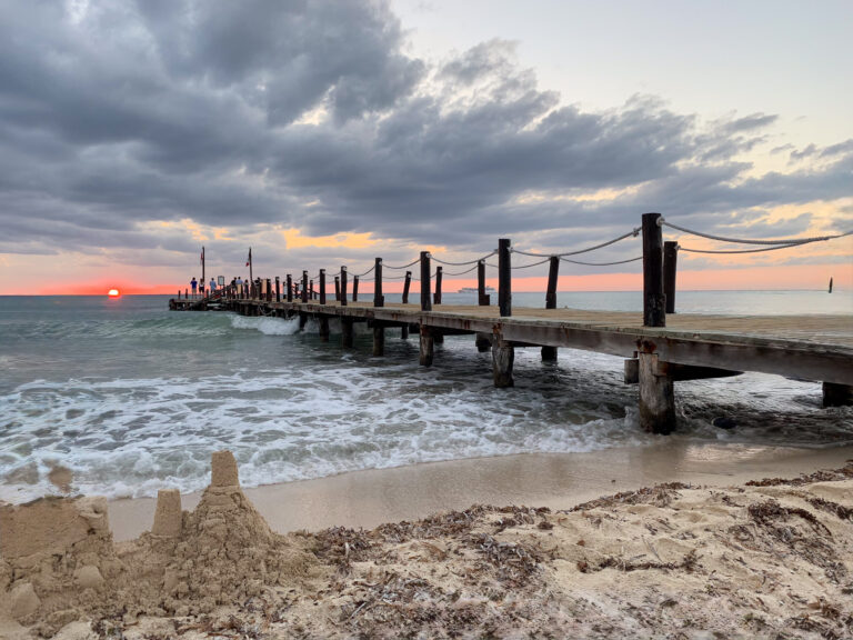 A small sandcastle in the foreground, the pier receding into a grey evening