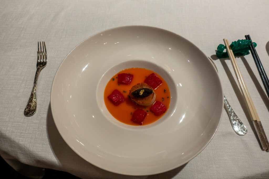 A small round dish in an orange-red sauce on a wide-rimmed white plate