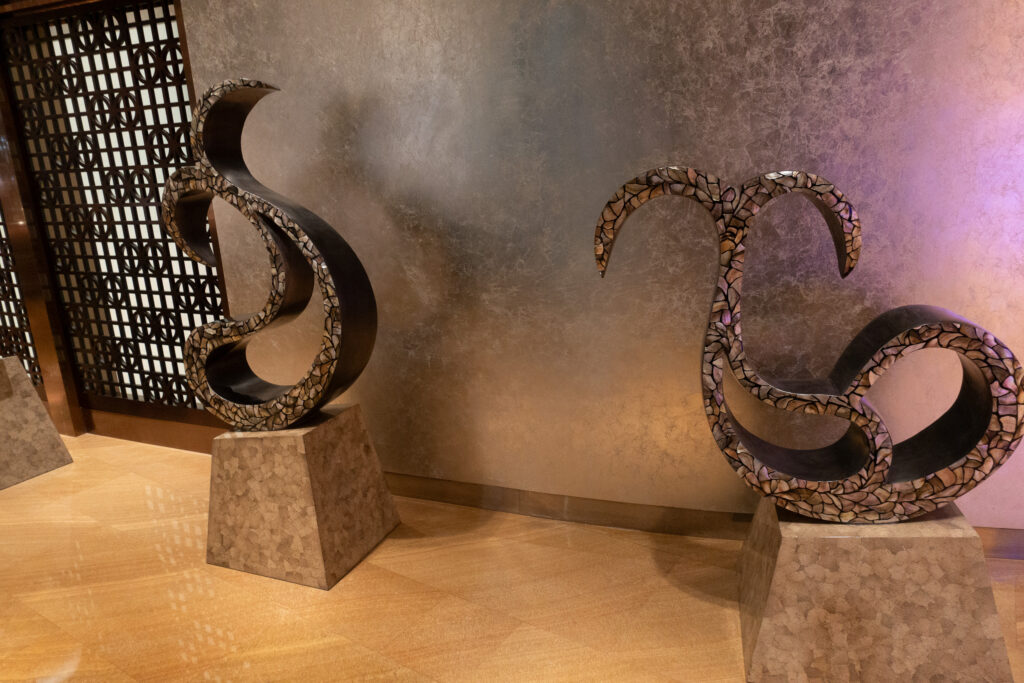 Two bronze dragon sculptures on stone plinths against a bronze wall beside a dark lattice screen at the restaurant entrance