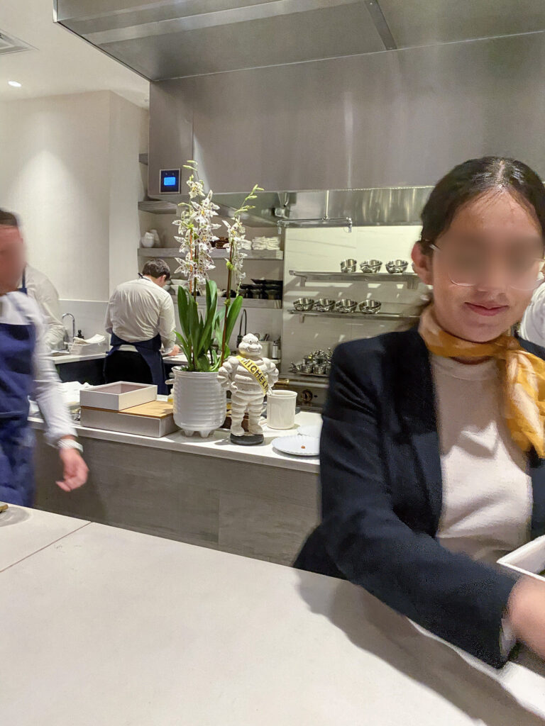 A guest seated at the counter with the open kitchen behind, a Michelin figure on the pass