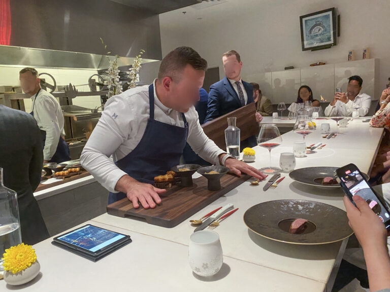 The chef presenting a board across the counter to the seated guests