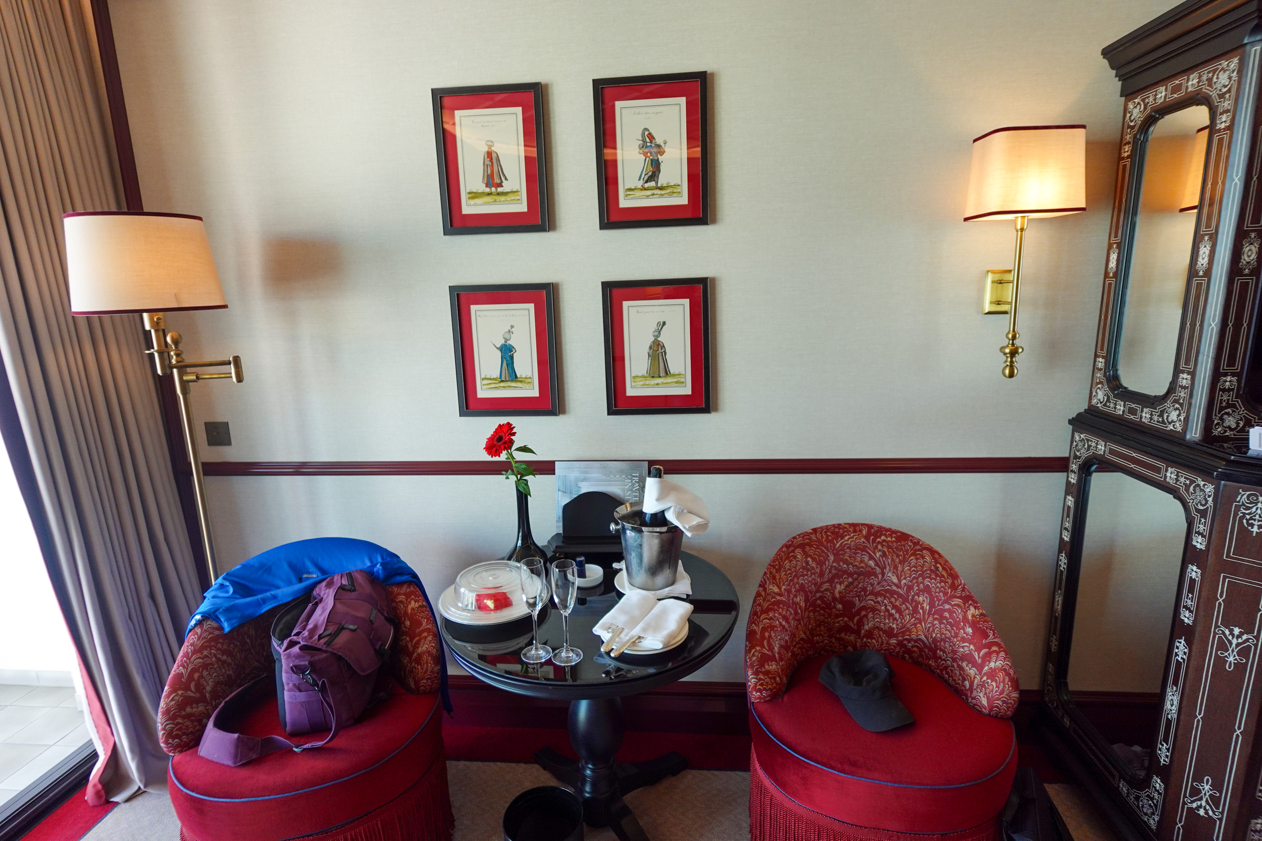 Two red tub chairs at a round table with an ice bucket, framed Ottoman prints on the wall above
