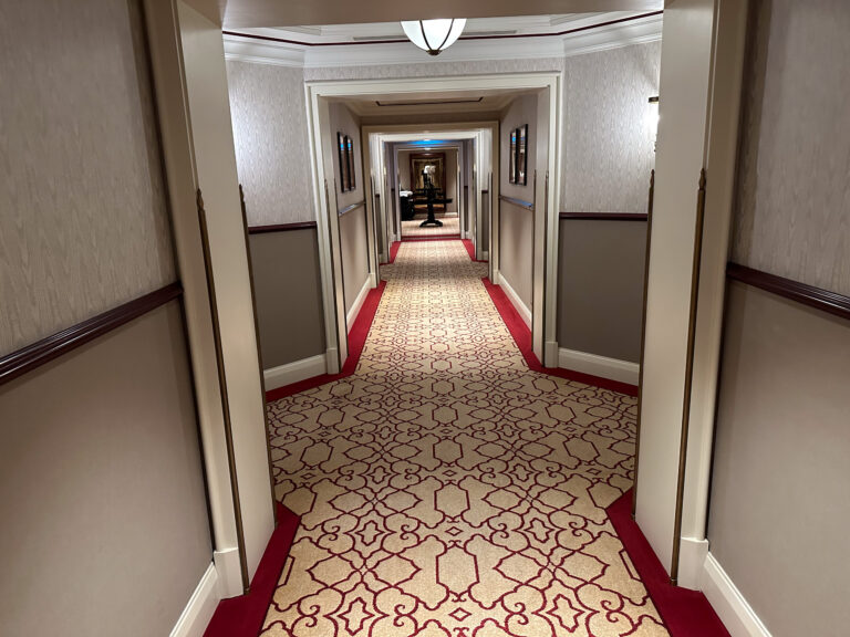 A long corridor with a patterned red and cream carpet running towards a lit window