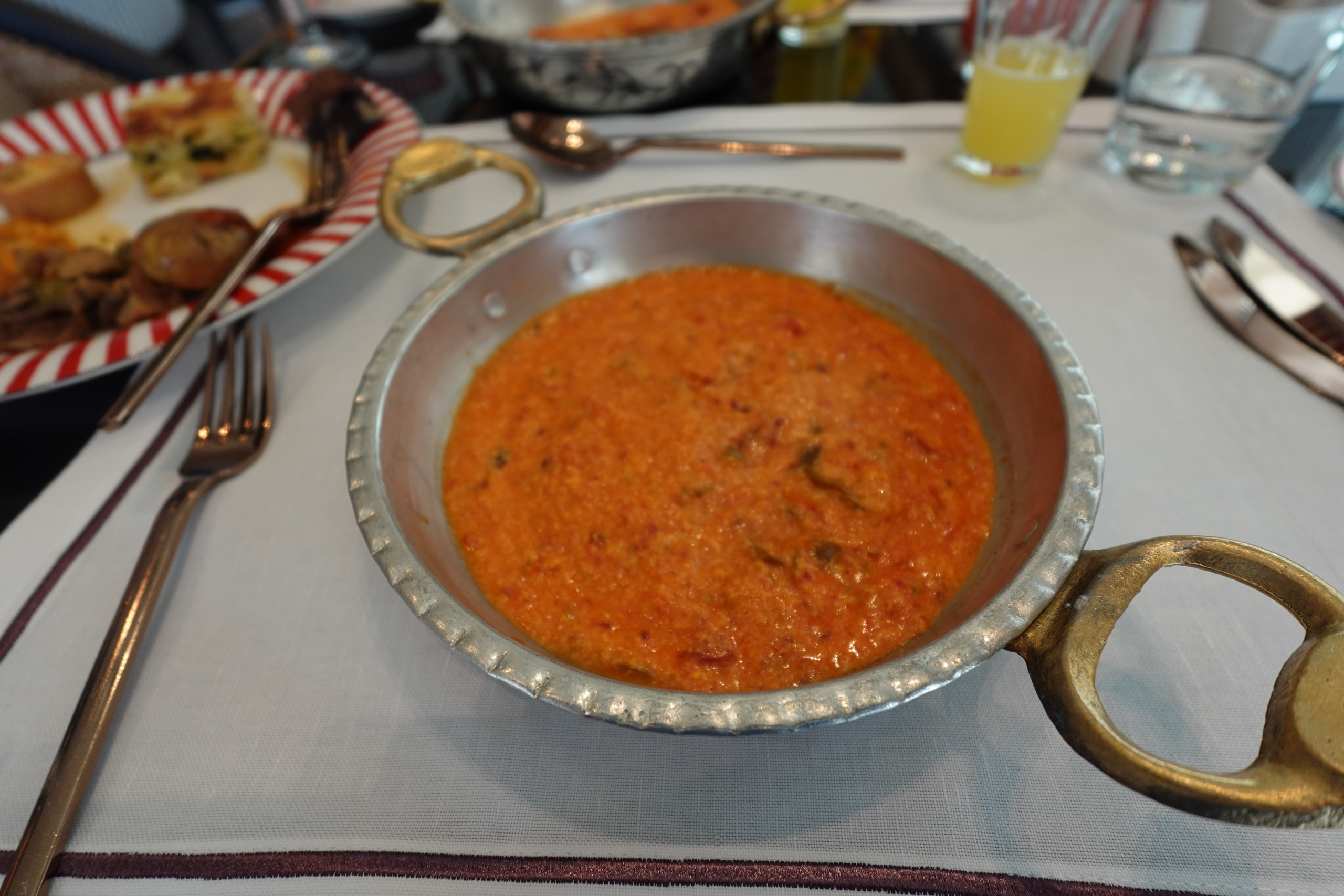 A copper pan of tomato and egg at the breakfast table, plates and juice set around it