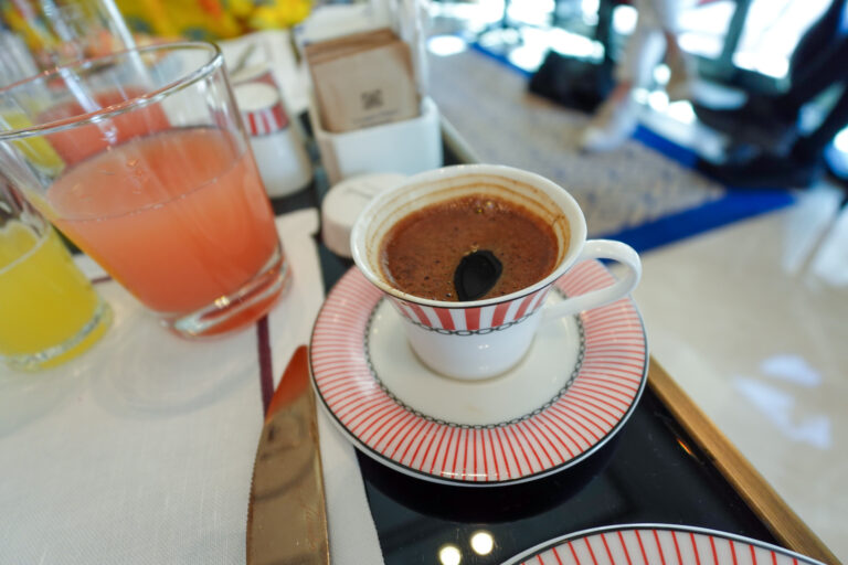 A cup of Turkish coffee in a red-striped cup and saucer beside two glasses of juice