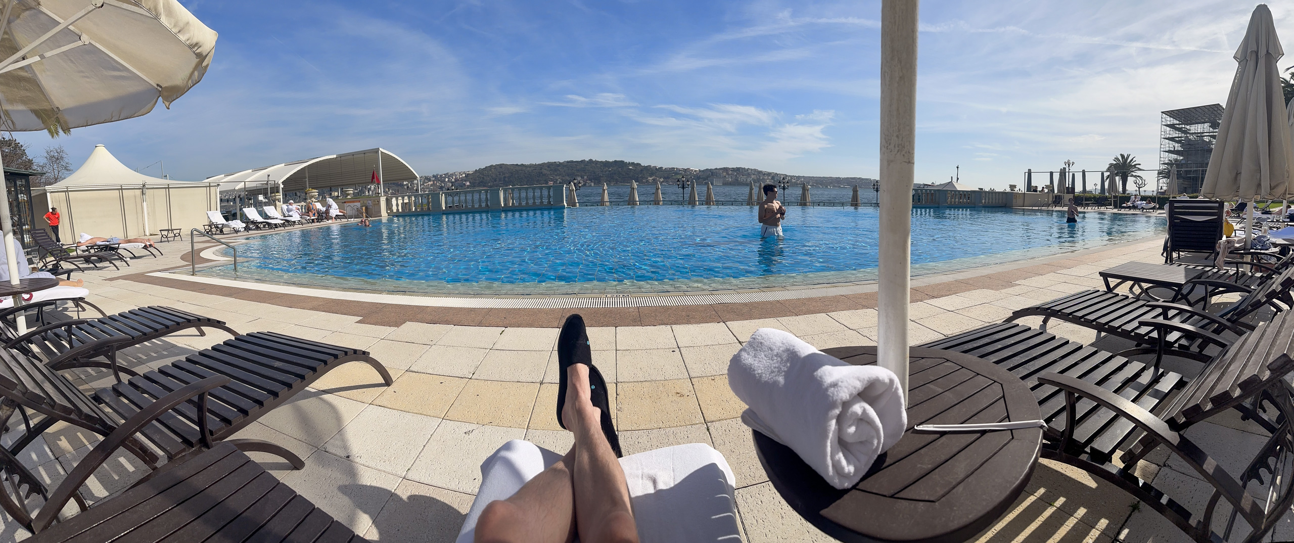 The long outdoor pool seen from a sun lounger, a rolled towel on the chair alongside