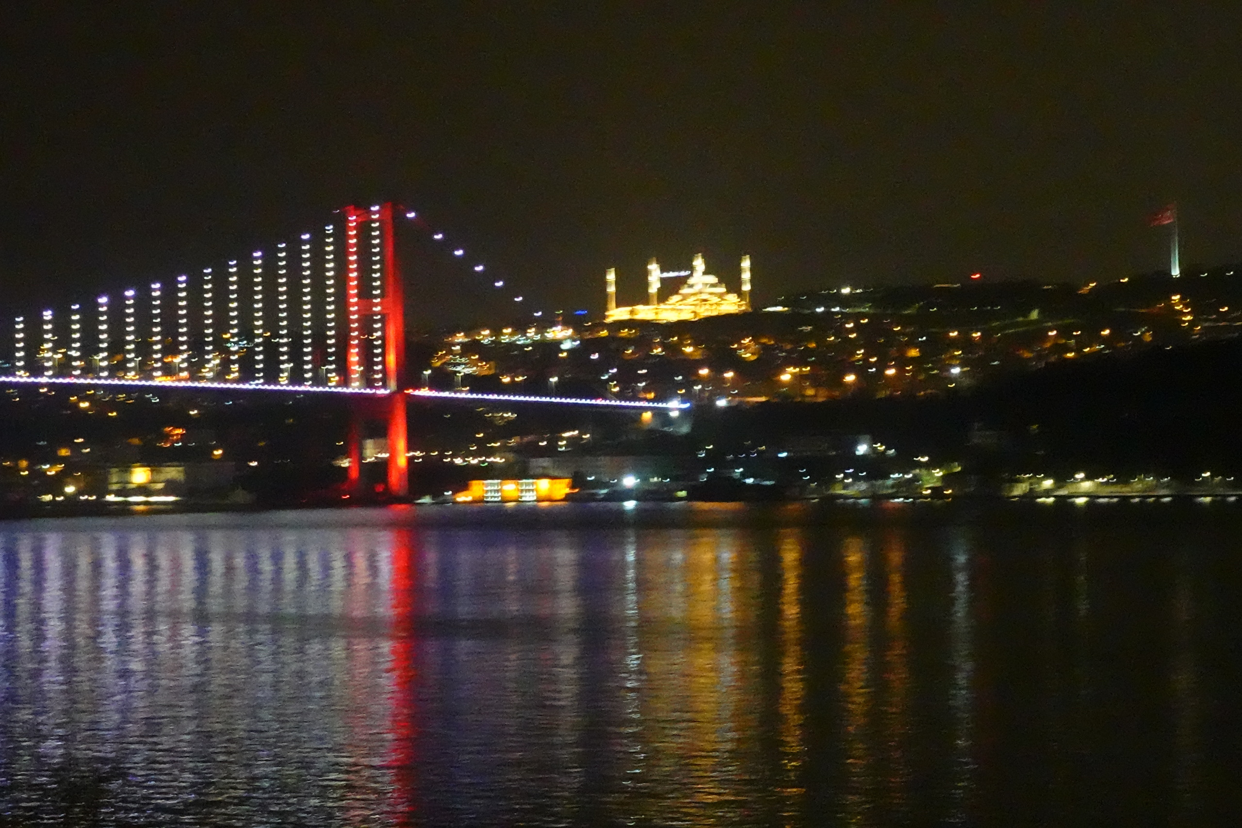 The suspension bridge lit red across the Bosphorus at night, a floodlit mosque on the far shore