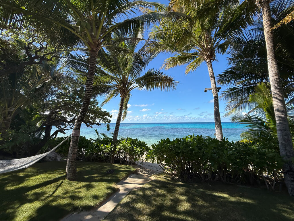 Coconut palms and a hammock on a mown lawn above the beach, turquoise water and a reef line beyond
