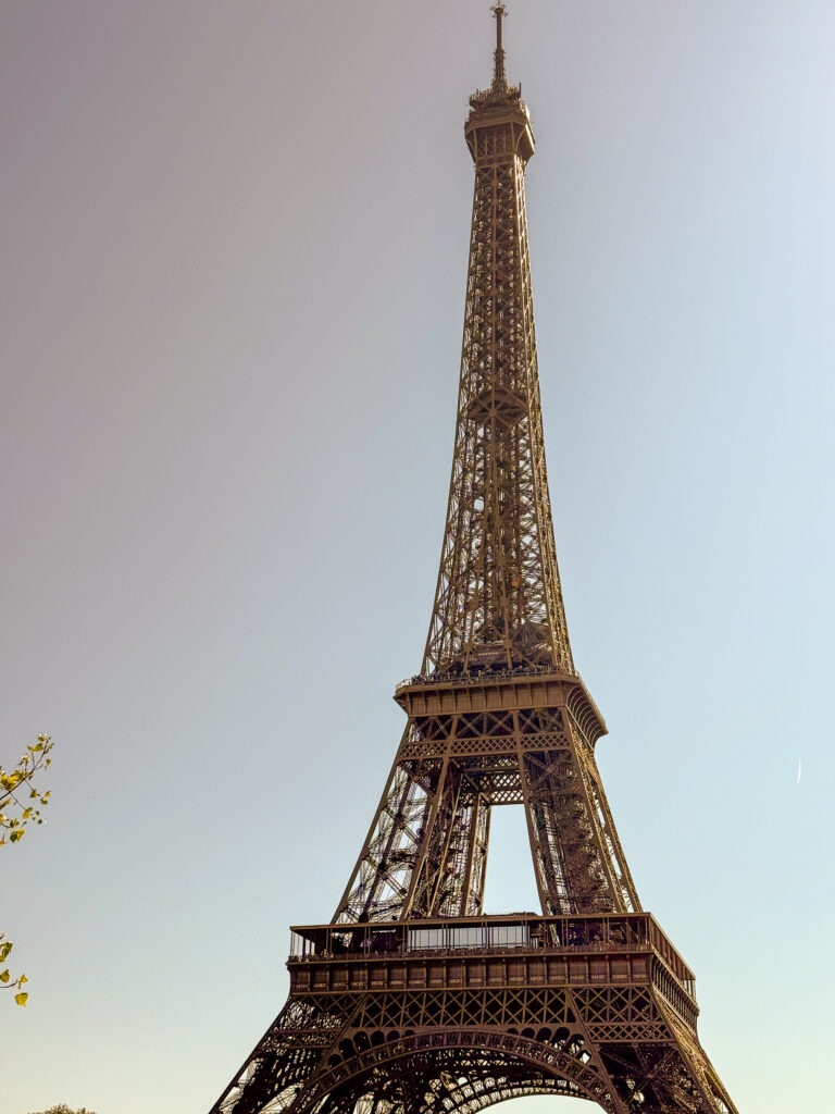 The Eiffel Tower seen from below against a clear pale sky