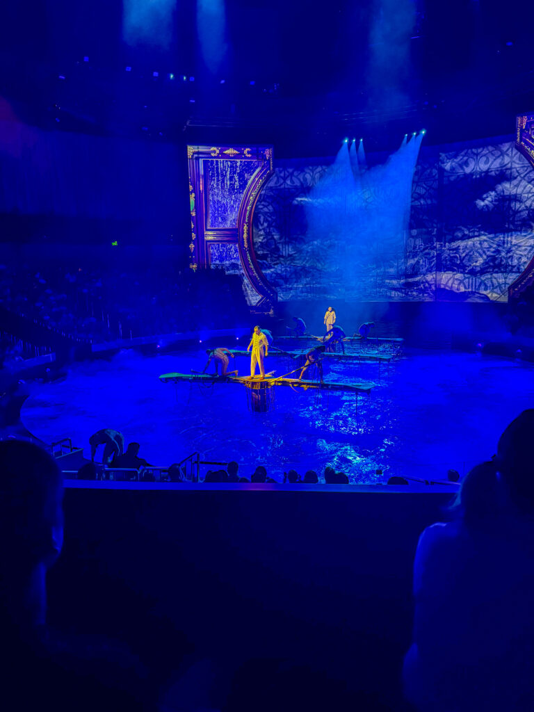 A performer above the water stage in blue light