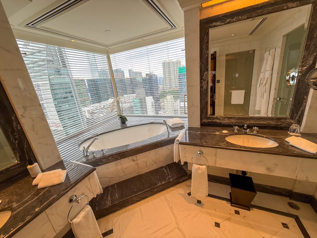 A marble bathroom at The Peninsula with a tub set into the corner window and the Hong Kong skyline across the harbour beyond