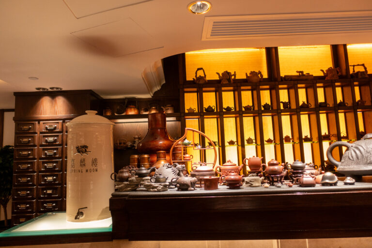 A lit display of teapots and canisters behind a lacquered counter