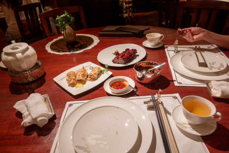 Dumplings and small plates on a red lacquer table with a pot of tea