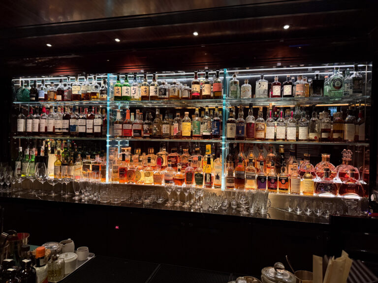 A long back-bar of bottles lit from beneath, glassware ranged along the counter