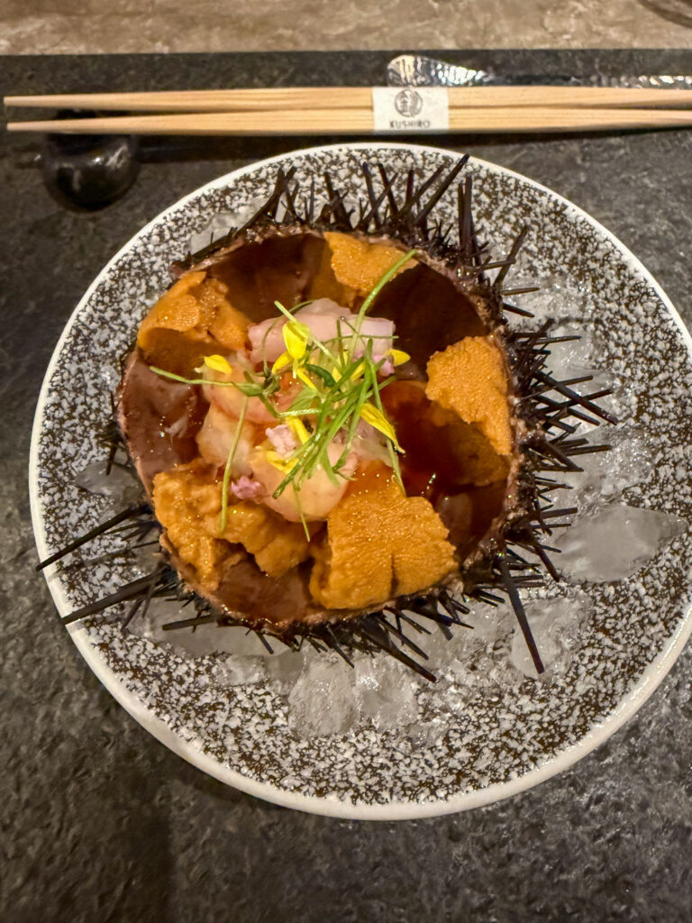 A dish of urchin and diced fish served in its shell over crushed ice