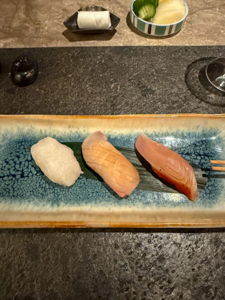 Three pieces of nigiri on a pale glazed board