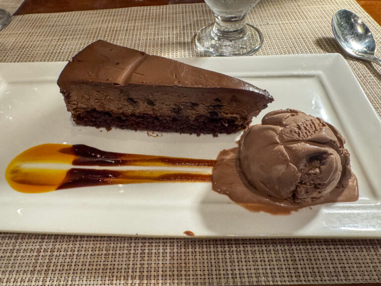 A wedge of chocolate cake with ice cream and a drawn sauce